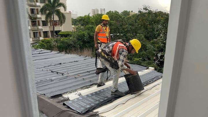 Applicators working with a bitumen pot on a metal roof